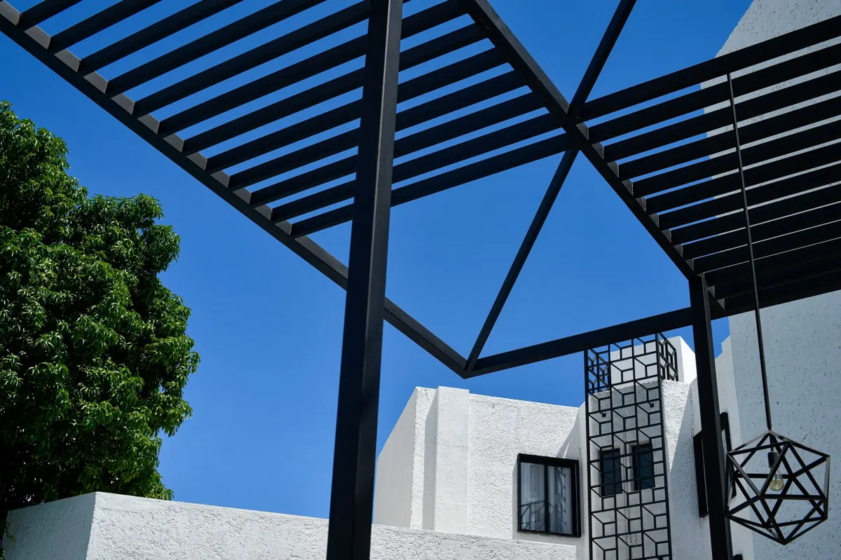 Pérgola de estructura oscura frente a una casa blanca